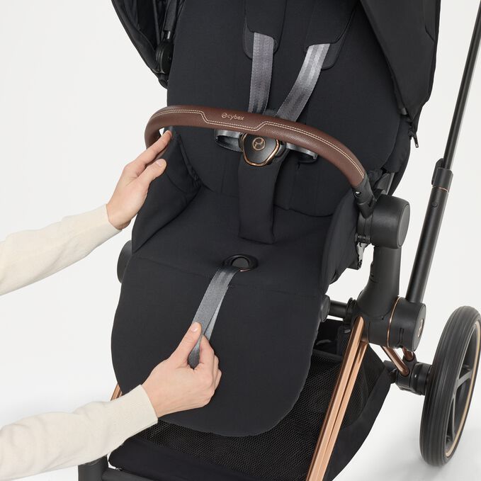 Elegancki wózek Cybex Priam 5.0 w trybie spacerowym, prowadzony przez stylowo ubraną mamę na zadbanej, miejskiej alei, skąpany w łagodnym świetle słonecznym